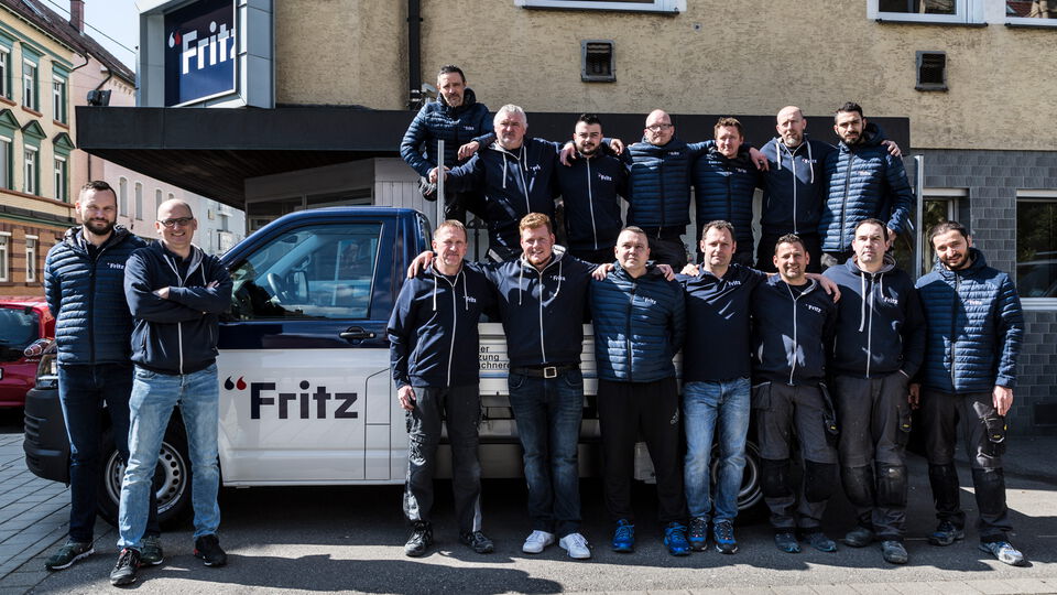 Das Fritz Team steht lächelnd vor dem Firmenwagen und präsentiert stolz ihre Zusammenarbeit.