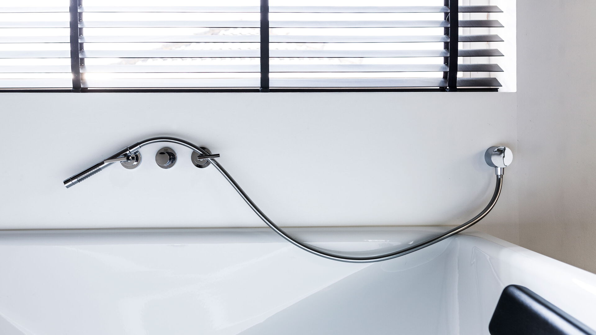 Eine weiße Badewanne vor einem Fenster mit Jalousien.